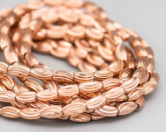 May include: A close-up of a strand of rose gold colored beads. The beads are oval shaped and have a wavy texture.