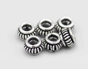 May include: A group of six silver metal beads with a decorative, textured design. The beads are round and have a hole in the center.