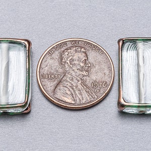May include: Three clear glass beads with copper and green trim. The beads are rectangular and have a slightly rounded edge. The beads are about the size of a US penny.