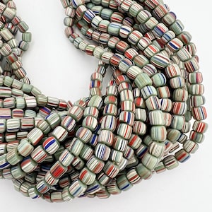 May include: A close-up of a strand of colorful glass beads. The beads are a mix of white, green, red, and blue. The beads are all cylindrical and have a smooth, polished finish.