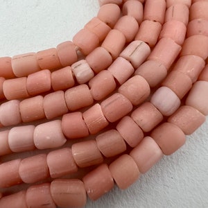 May include: A strand of pink glass beads, each bead is cylindrical and slightly rounded on the ends. The beads have a frosted, matte finish.