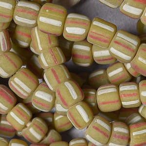 May include: A close-up of a string of yellow and white striped glass beads with red accents. The beads are cylindrical and have a matte finish.