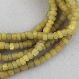 May include: A close-up of a strand of yellow glass beads. The beads are small and round, and they are strung together on a clear thread.
