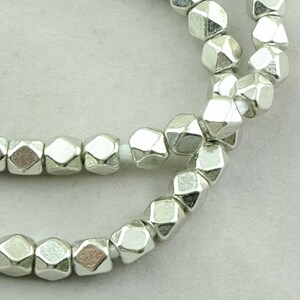 May include: A strand of silver-toned metal beads. Each bead is faceted and has a geometric shape.