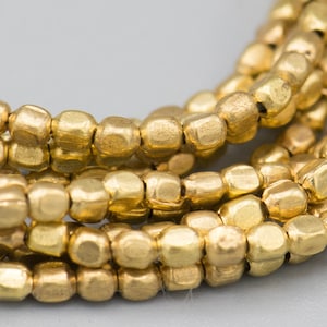 May include: A close-up of a strand of gold-colored beads. The beads are small and have a hammered texture. They are arranged in a loose pile, with some of the beads overlapping.