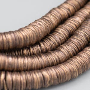 May include: A close-up of a strand of brown metal beads. The beads are round and have a hammered texture.