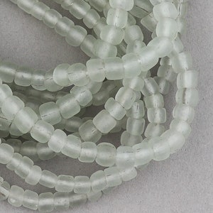 May include: A strand of light green glass beads. The beads are small and round, and they have a frosted finish.