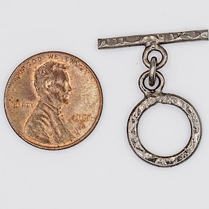 May include: Silver toggle clasp with a textured finish. The clasp has a round ring and a bar with a textured finish. The clasp is about the size of a US penny.
