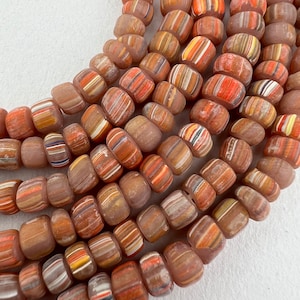 May include: A strand of colorful glass beads with a layered, striped pattern in shades of brown, orange, and white. The beads are opaque and have a slightly frosted finish.