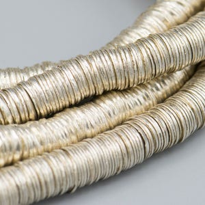 May include: A close-up of a silver chain made of many small, round, and textured metal beads. The beads are stacked on top of each other to create a long, continuous chain.