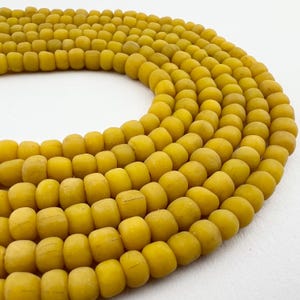 May include: A close-up of a strand of yellow glass beads. The beads are round and have a matte finish. They are arranged in a circular pattern.