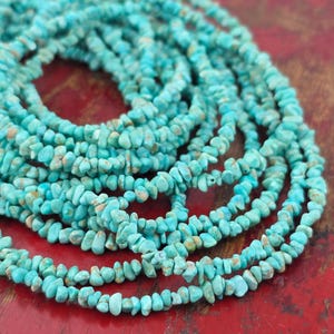 May include: A long strand of small, irregular turquoise gemstone chips. The beads are a vibrant, bright blue-green color with natural brown matrix inclusions, strung together to form a continuous, coiled necklace of raw, tumbled stone pieces.