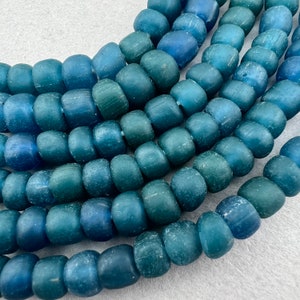 May include: A strand of blue glass beads with a frosted finish. The beads are round and have a slight variation in color, ranging from a light to a dark blue.