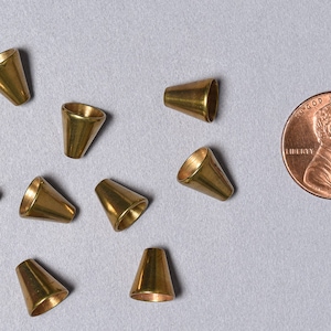 Puede incluir: Diez cuentas de metal de color dorado en forma de cono, aproximadamente del tamaño de una moneda de un centavo de euro.