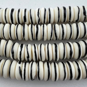 May include: White and black striped round beads. The beads are made of bone and have a glossy finish.