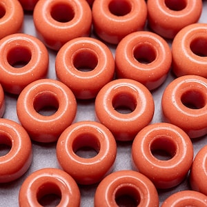 May include: A close-up of a group of orange ceramic beads. The beads are round with a hole in the centre. They are arranged in a random pattern.