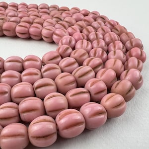 May include: A strand of pink glass beads with a ribbed texture. The beads are round and have a matte finish.