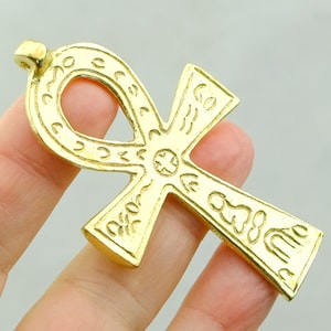 May include: A gold-colored Ankh pendant with intricate details. The pendant is made of metal and has a loop at the top for hanging.