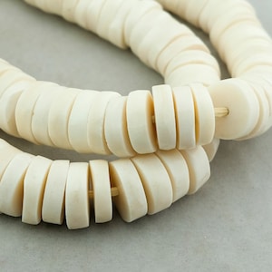 May include: A strand of white, round, flat beads, strung together on a thin cord. The beads are stacked on top of each other, creating a layered effect.