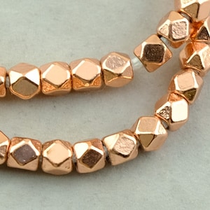 May include: Two strands of copper-colored faceted beads. The beads are hexagonal in shape and have a metallic finish.