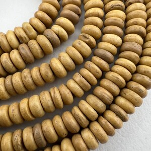 May include: A close-up of a strand of light brown, natural wood beads. The beads are round and have a slightly rough texture.