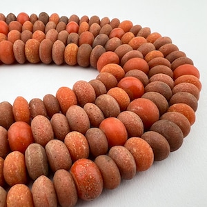 May include: A strand of orange and brown round beads. The beads are made of a rough, textured material.