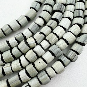 Peut inclure: Gros plan sur des rangées de perles en forme de baril, grises et noires. Les perles présentent un motif rayé et sont enfilées avec des intercalaires noirs. Ces perles aux tons neutres peuvent être utilisées pour la création de bijoux ou d'autres travaux manuels.