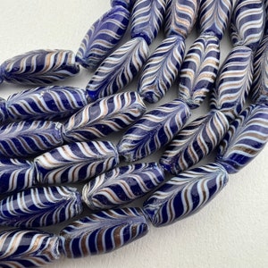 May include: A close-up of a collection of blue and white glass beads with a swirling pattern. The beads are oval shaped and have a glossy finish.