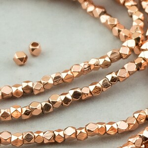 May include: A strand of rose gold faceted beads. The beads are small and have a geometric shape. There are also three loose beads in the image.