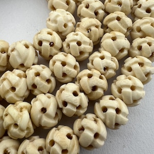May include: A close-up of a collection of off-white, intricately carved bone beads. The beads are spherical and have a woven pattern.