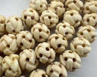 May include: A close-up of a collection of off-white, intricately carved bone beads. The beads are spherical and have a woven pattern.