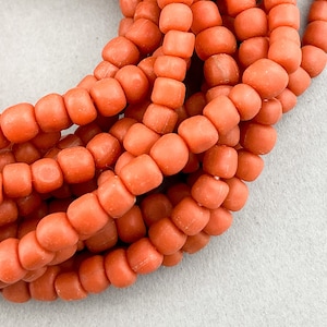 May include: A close-up of a strand of orange glass beads. The beads are round and have a matte finish.