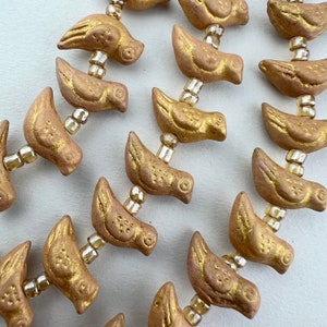 May include: A strand of gold-colored ceramic bird beads with a textured surface. The beads are strung on a wire with small, clear beads between each bird.