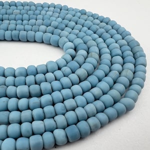 May include: A close-up of a strand of light blue round beads. The beads are made of a smooth, matte material and are arranged in a circular pattern.