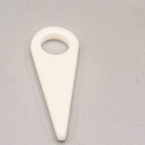 May include: White plastic tool with a loop at the top and three holes down the center. The tool is shaped like a triangle with a rounded point.