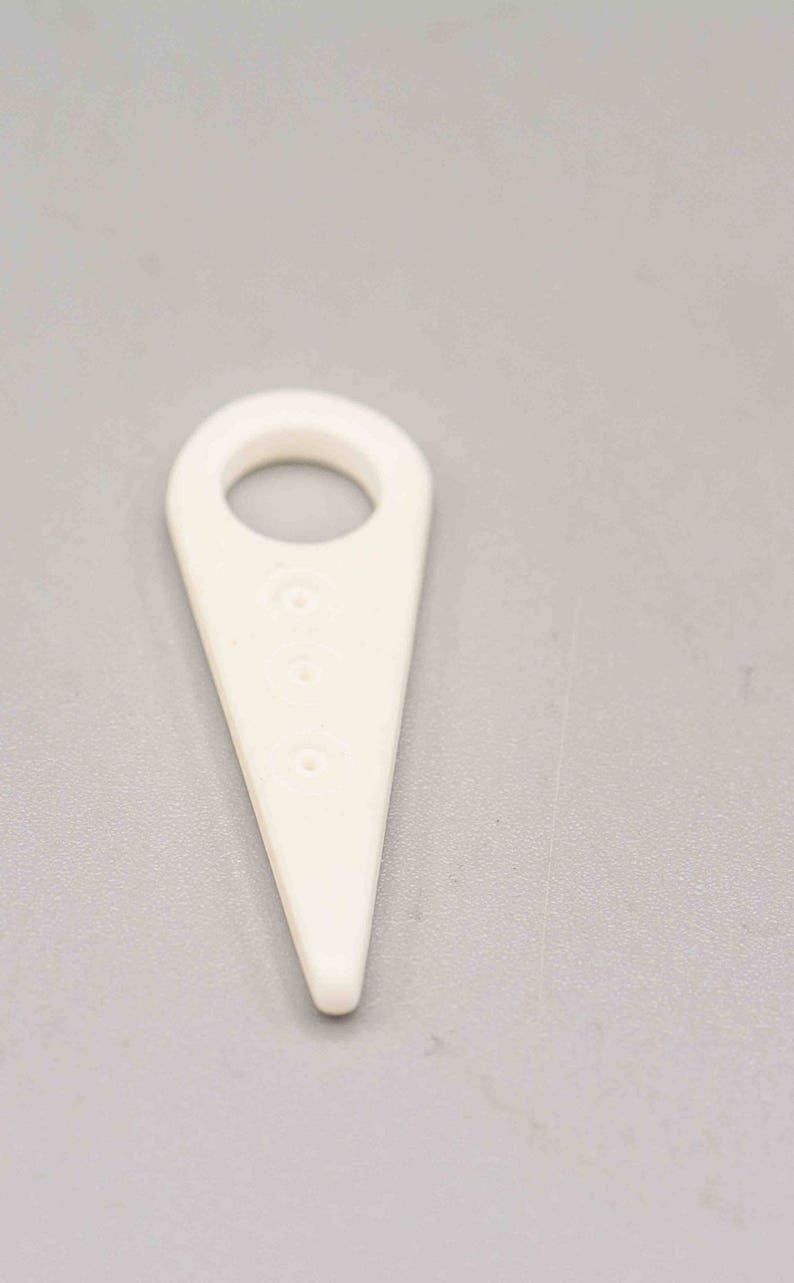 May include: White plastic tool with a loop at the top and three holes down the center. The tool is shaped like a triangle with a rounded point.