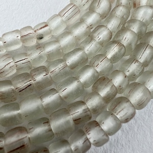May include: A close-up of a strand of frosted glass beads with a subtle brown stripe pattern. The beads are opaque and have a slightly irregular shape.