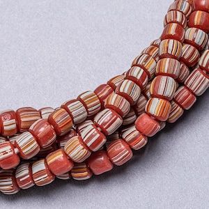 May include: A close-up of a strand of red, white and orange striped glass beads. The beads are cylindrical and have a slightly irregular shape.