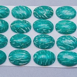 May include: A sheet of 16 oval-shaped green amazonite cabochons with white streaks. The cabochons are arranged in four rows of four. A penny is included for scale.