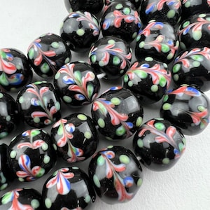 May include: A strand of black glass beads with white, red, and blue swirl designs. The beads are round and have a glossy finish.