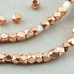 May include: A strand of rose gold faceted beads, with a few loose beads scattered nearby. The beads are small and have a geometric shape.