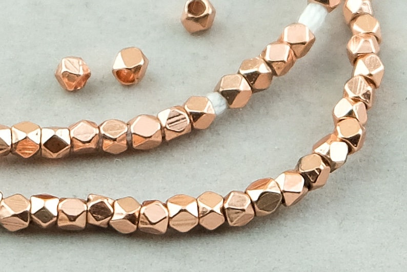 May include: A strand of rose gold faceted beads, with a few loose beads scattered nearby. The beads are small and have a geometric shape.