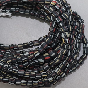 May include: A close-up of a long strand of black, white and red beads. The beads are made of glass and have a cylindrical shape. The beads are arranged in a random pattern.