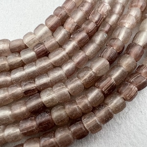 May include: Close-up of strands of translucent, barrel-shaped beads in varying shades of brown and tan. The beads have a slightly irregular shape and are strung together, creating a textured surface. Ideal for jewelry making.
