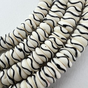 May include: A close-up of a strand of white and black zebra patterned beads. The beads are round and have a glossy finish.