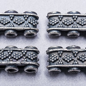 May include: Four silver-toned metal beads with a geometric pattern. Each bead has three connected sections, creating a rectangular shape.