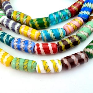 May include: Close-up of a strand of colorful glass beads. The beads are cylindrical with a variety of colors and patterns, including blue, green, yellow, red, and white. The beads have a swirled design.