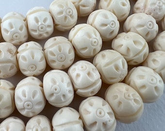 May include: A close-up of a string of white oval beads with a carved flower design. The beads are made of bone and have a smooth, polished finish.