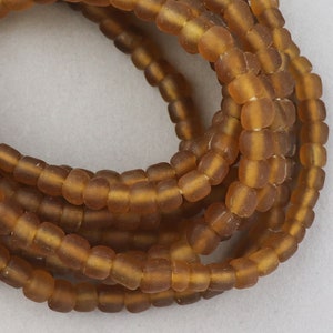 May include: Strands of amber-colored, square-shaped beads. The beads have a slightly frosted appearance and are strung together, creating a coiled pattern. The beads are a warm, earthy tone, suggesting a natural material.
