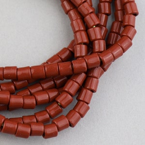 May include: A strand of terracotta-colored ceramic beads. The beads are cylindrical and have a smooth, glossy finish.